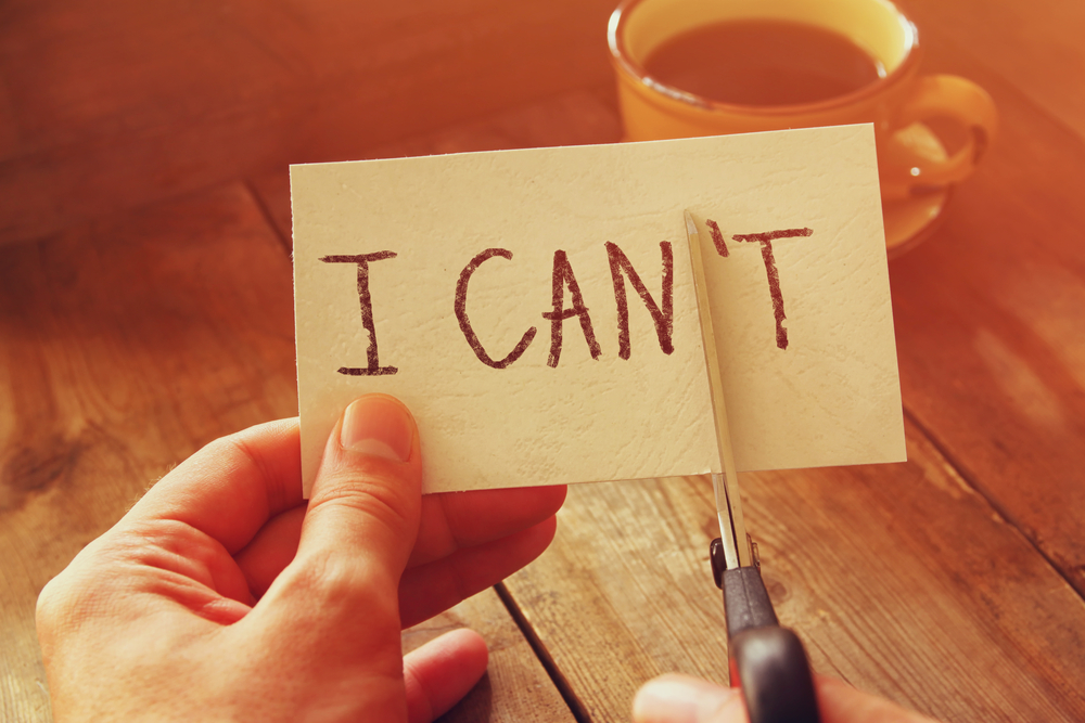 「I CAN'T」と書かれたカードの「N'T」の部分をハサミで切り取る人の手元