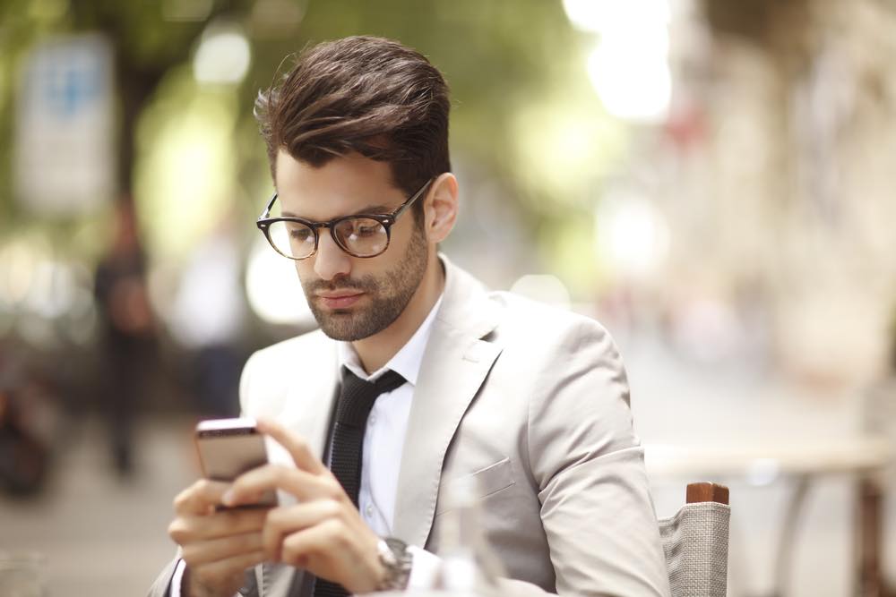 スマートフォンを見る眼鏡をかけてスーツを着た男性