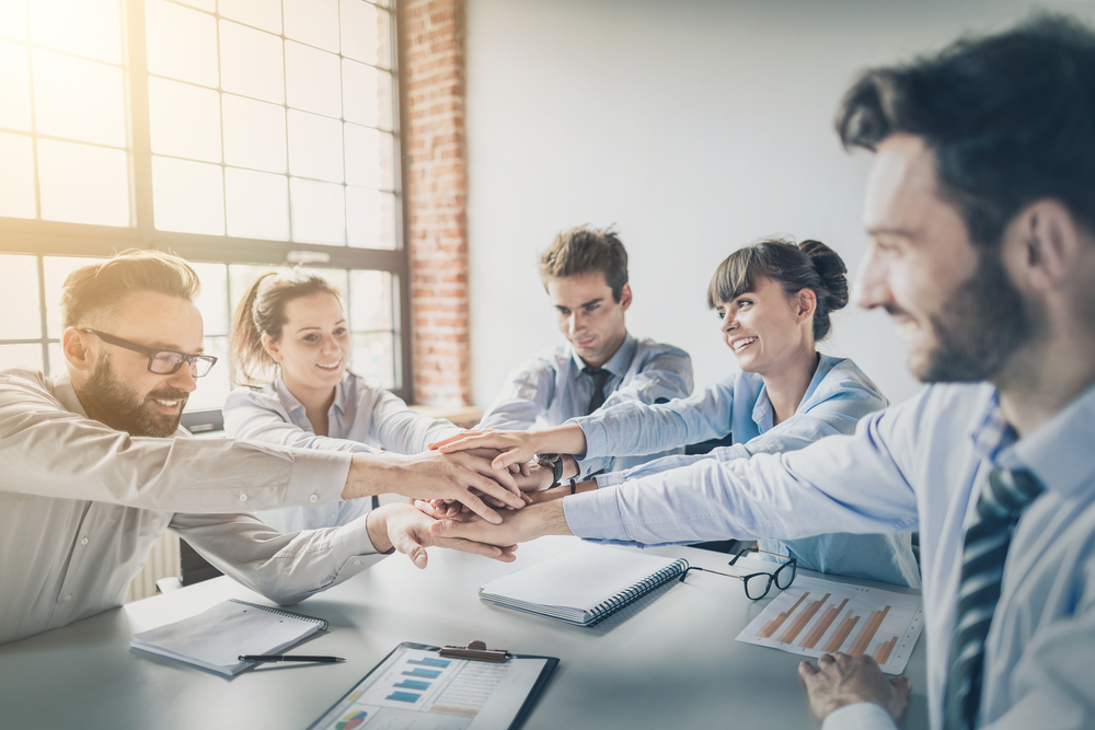 会議室の机の上で手を重ね合わせる人々