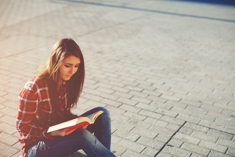 道に座り込んで本を読む女性