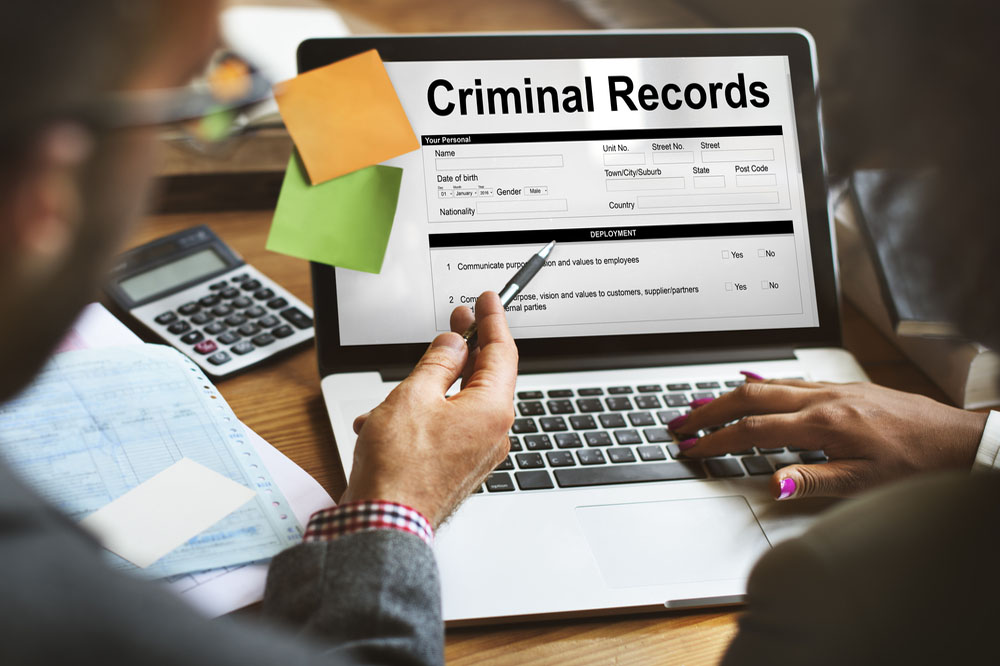 「Criminal Records」を表示したノートパソコンとそれを見る人達
